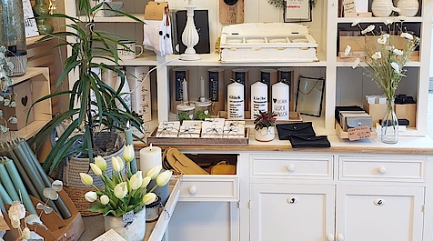 Geschmackvoll eingerichteter Ladenbereich in weißem Schrank, Kerzen, Vasen, Pflanzen, Geschirr und dekorativen Geschenkartikeln und weißen Tulpen