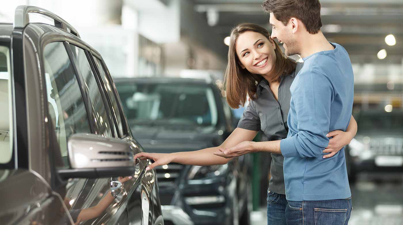 Paar betrachtet ein Auto in einem Autohaus, Frau zeigt auf die Fahrzeugtür.