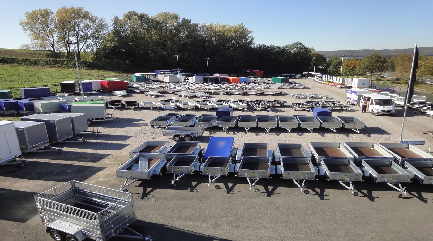 Großer Anhängerplatz mit verschiedenen Modellen und Farben, umgeben von Bäumen.